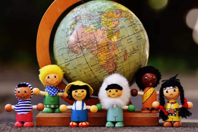 Small dolls looking like children in front of a tiny globe. Photo.
