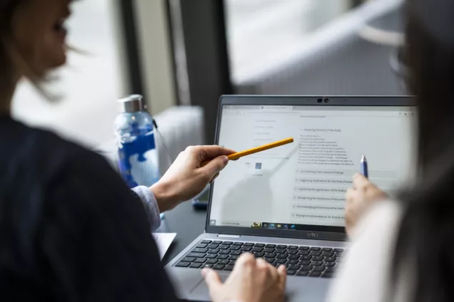 Person pointing at a laptop. Photo.