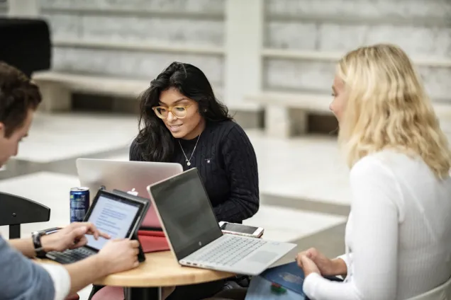 Students around a table with their laptops. 