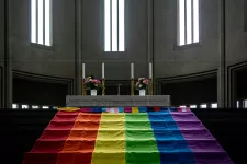 Foto på en prideflaggan draperad över trappan på altaret i en kyrka. 