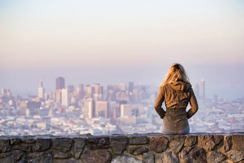 A girl sitting in front of a big city skyline. Photo.