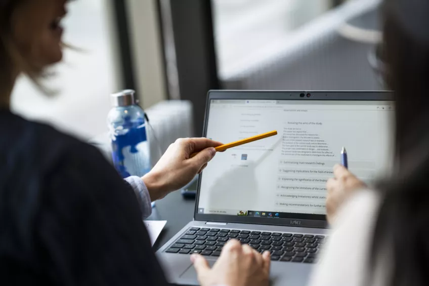 Person pointing at a laptop. Photo.