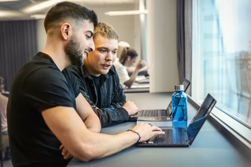 Two people are standing with a computer each. Photo.