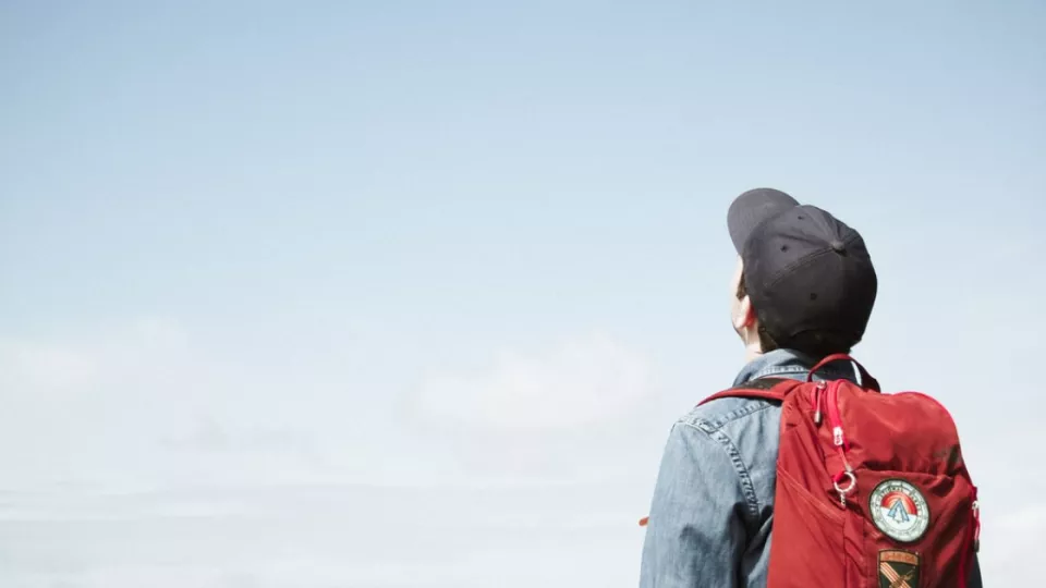 En ungdom med keps tittar upp mot en blå himmel.
