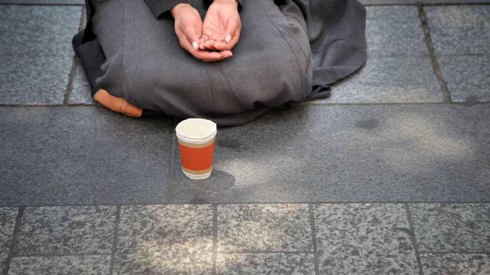 En människa sitter på marken med en mugg framför sig. Foto.