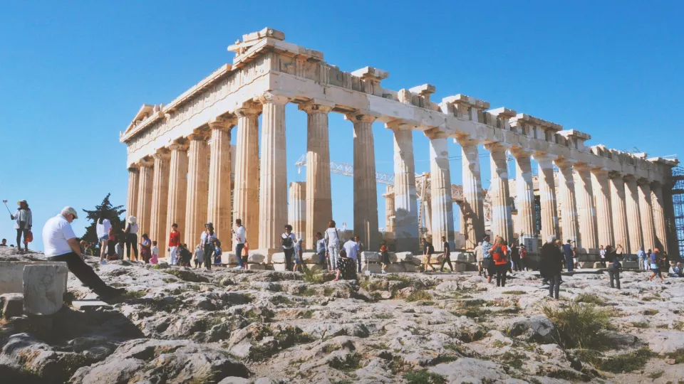 Flera turister står runt en vit byggnad från antikens Grekland. Foto.