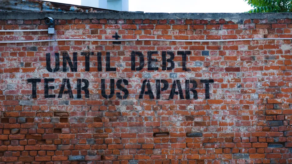 En tegelvägg med texten "Until debt tear us apart". Foto.
