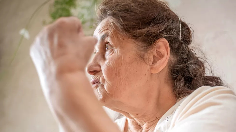 En äldre kvinna håller upp en knuten hand. Foto.
