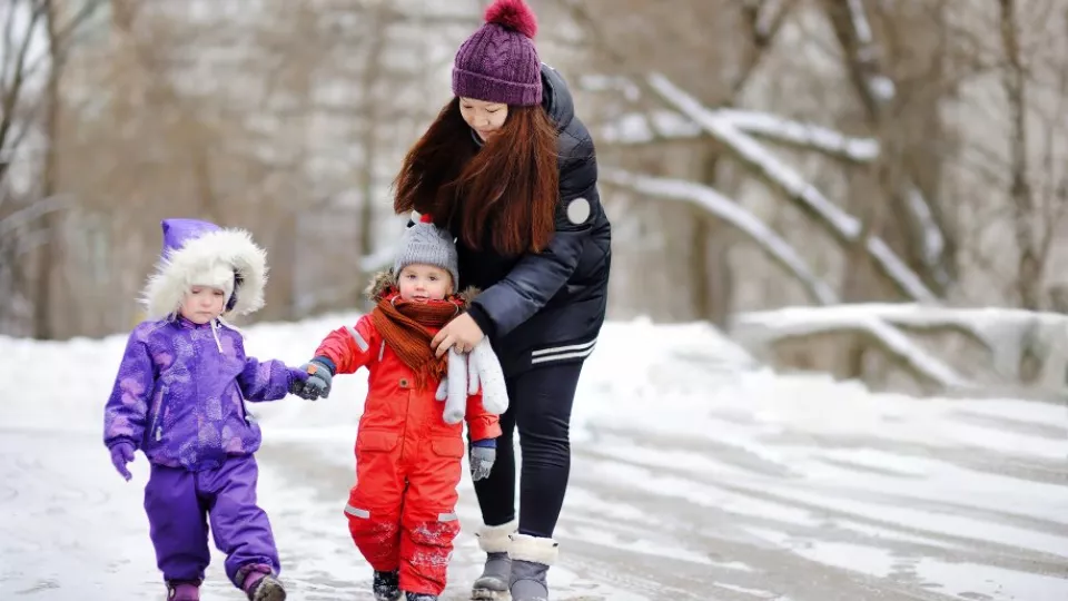 Ung kvinna går i vinterlandskap med två barn. Foto. 