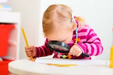 Ett barn sitter vid ett bord med ett förstoringsglas i ena handen och en penna i andra handen. Foto.