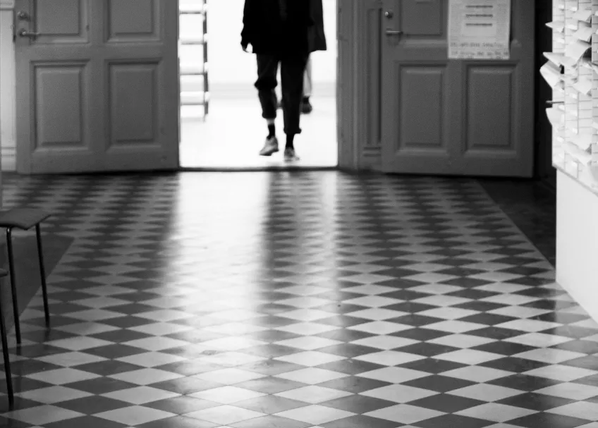 En ensam person går i en lång korridor. Svartvit bild.