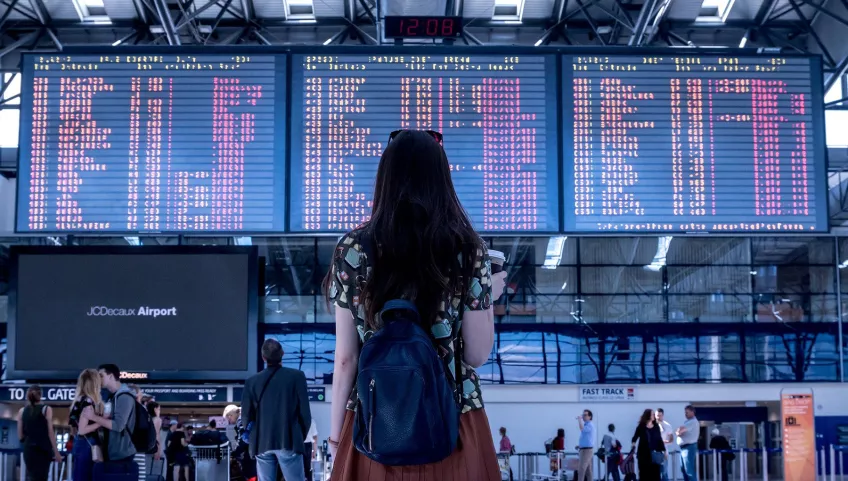 En kvinna står på en flygplats och tittar på en skärm med avgående flyg.