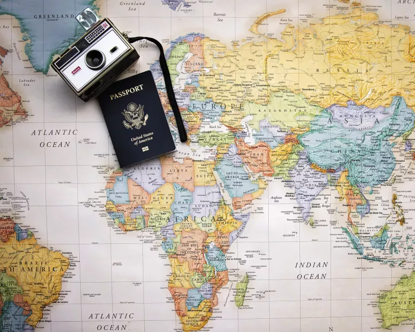Ett pass och en kamera som ligger på en världskarta. Foto.
